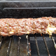 Meat log on the grill grates, turning brown and oozing some cheese out the side